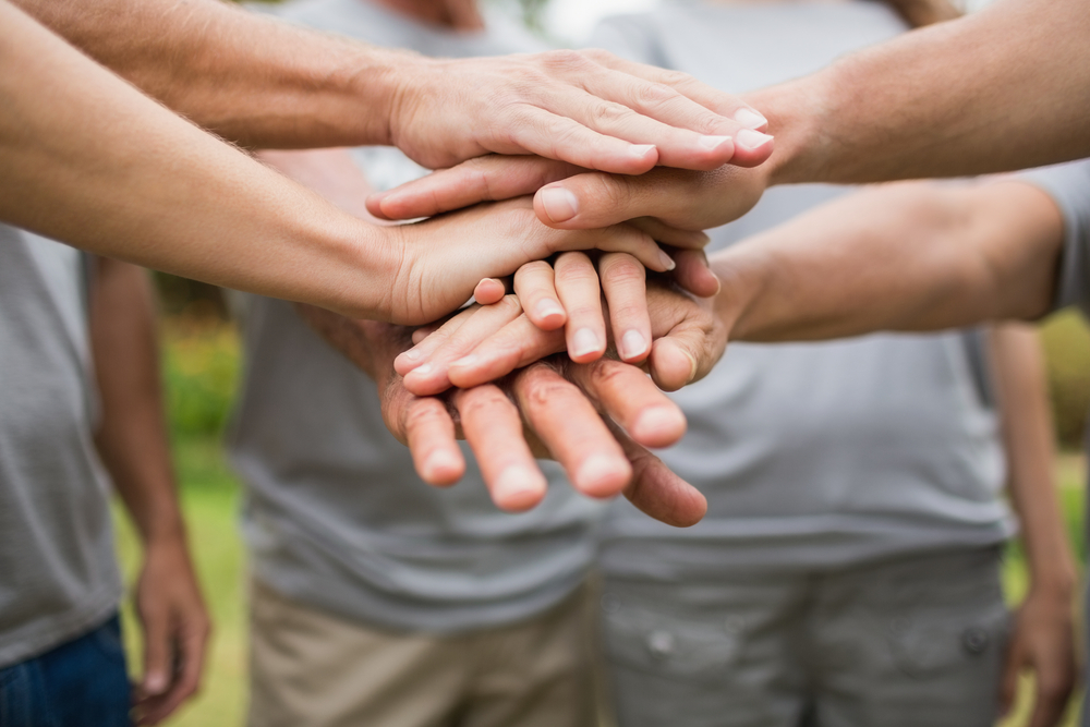 Happy volunteer family putting their hands together on a sunny day Happy volunteer family putting their hands together on a sunny day